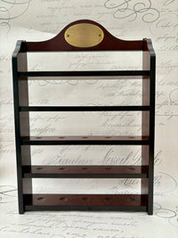 A cherry wood finish golf ball display shelf with black horizontal bars, featuring a brass plate at the top and another smaller one at the bottom.