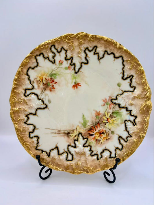Decorative ceramic plate with floral design and gold rim on a stand against a white background