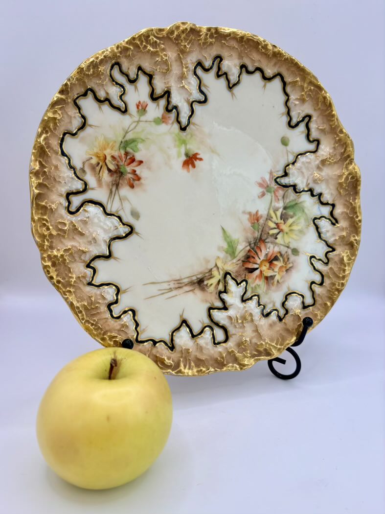 Decorative plate with floral design and gold rim next to a yellow apple on a white background
