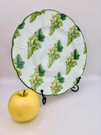 Decorative plate with green grape pattern on a stand, next to a yellow apple.