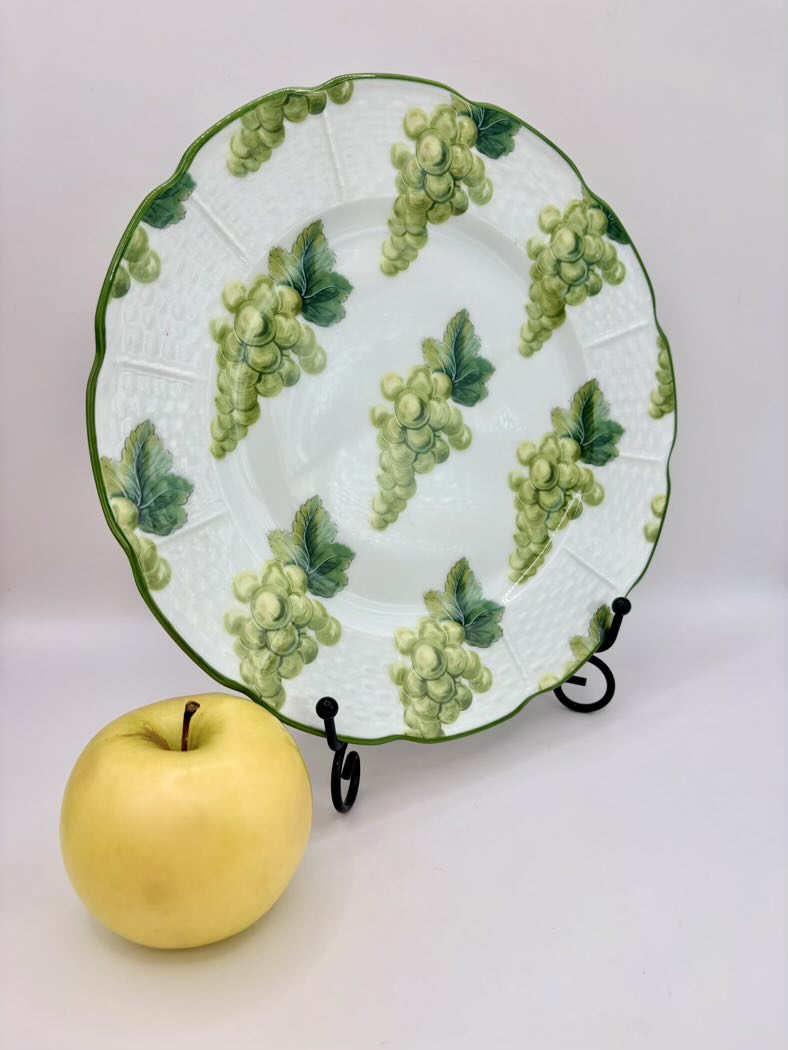 Decorative plate with green grape pattern on a stand, next to a yellow apple.