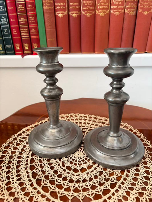Two metallic candlesticks on a doily with books in the background