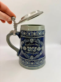 Decorative ceramic beer stein with blue and white patterns, held by a hand.