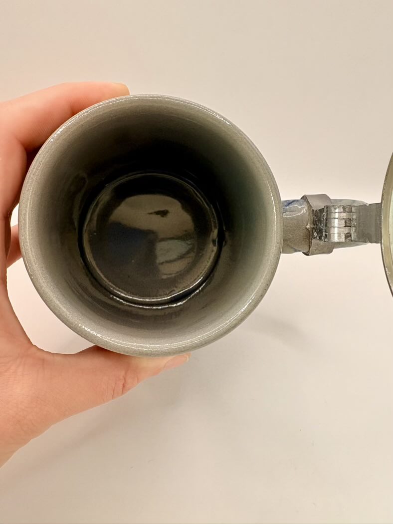 Person holding a ceramic mug with a metal handle against a plain background