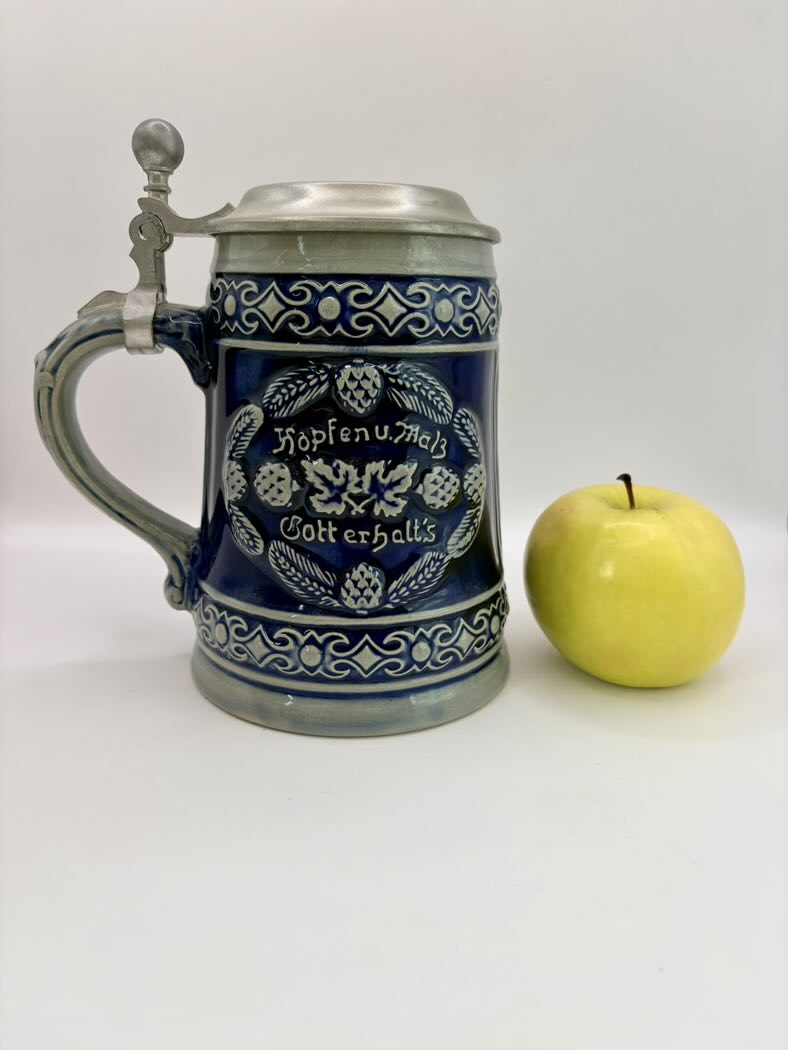 Decorative beer stein with blue design next to a yellow apple on a white background