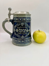 Decorative beer stein with blue design next to a yellow apple on a white background