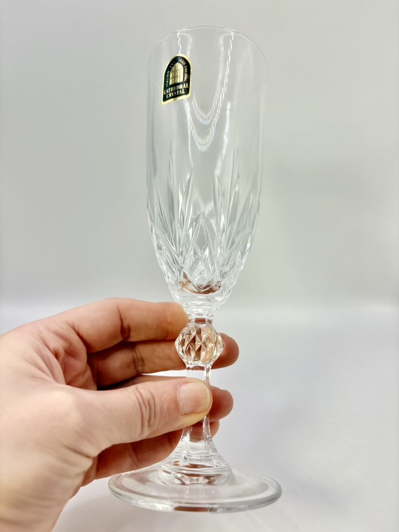 Clear glass flute held by a hand against a plain background