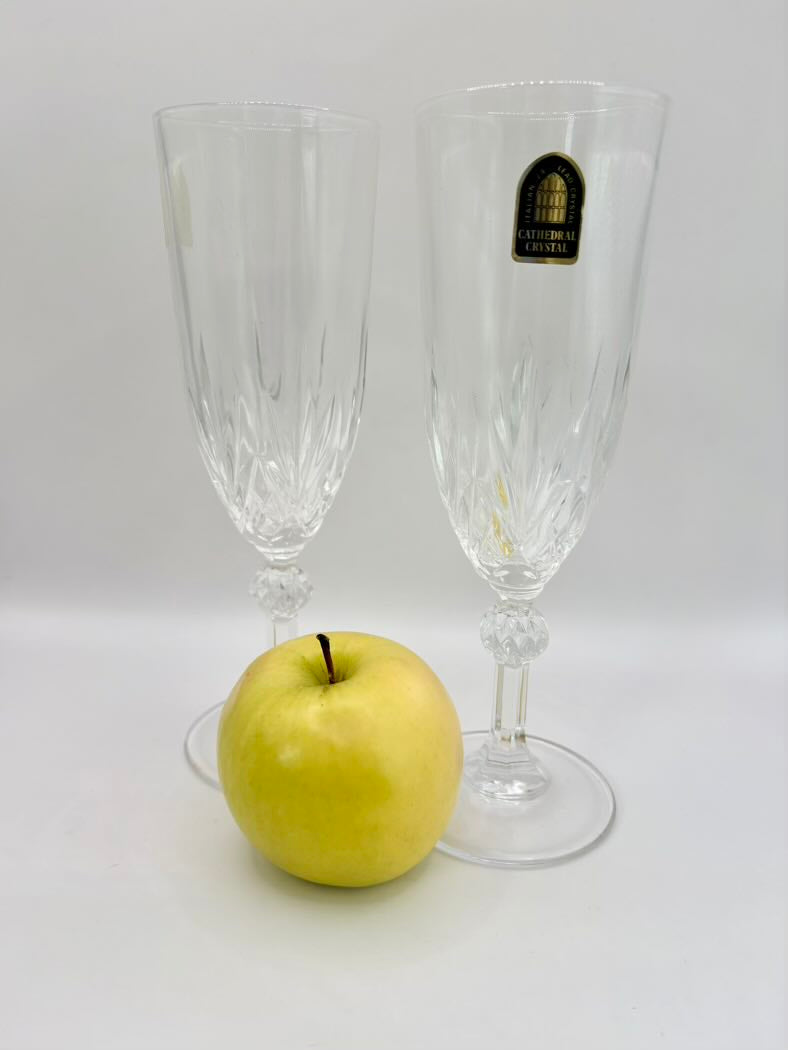 Two crystal champagne flutes with a gold apple on a white background