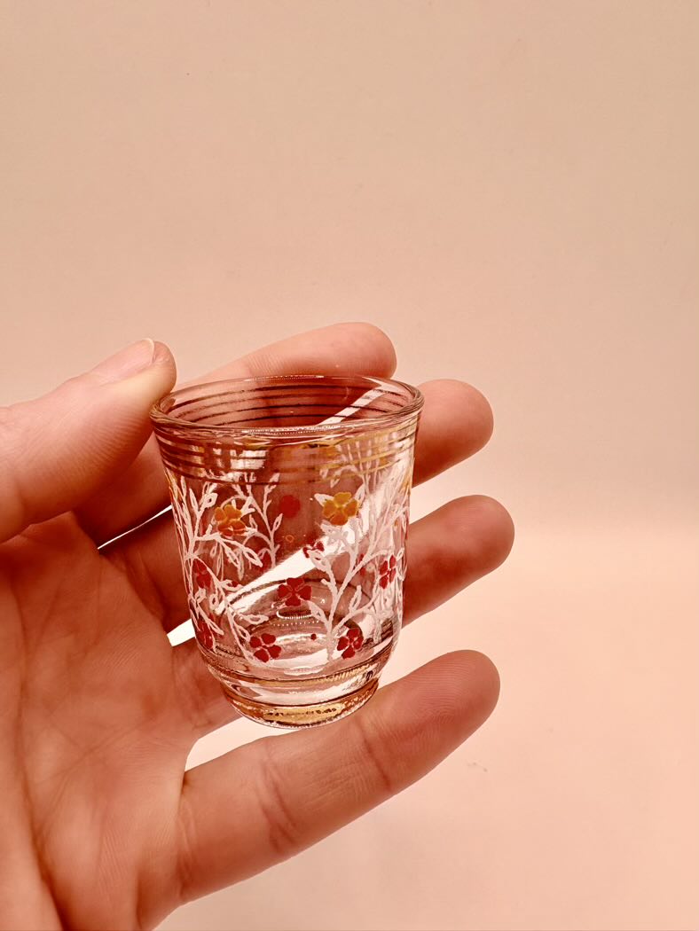 Hand holding a small glass with floral design against a beige background