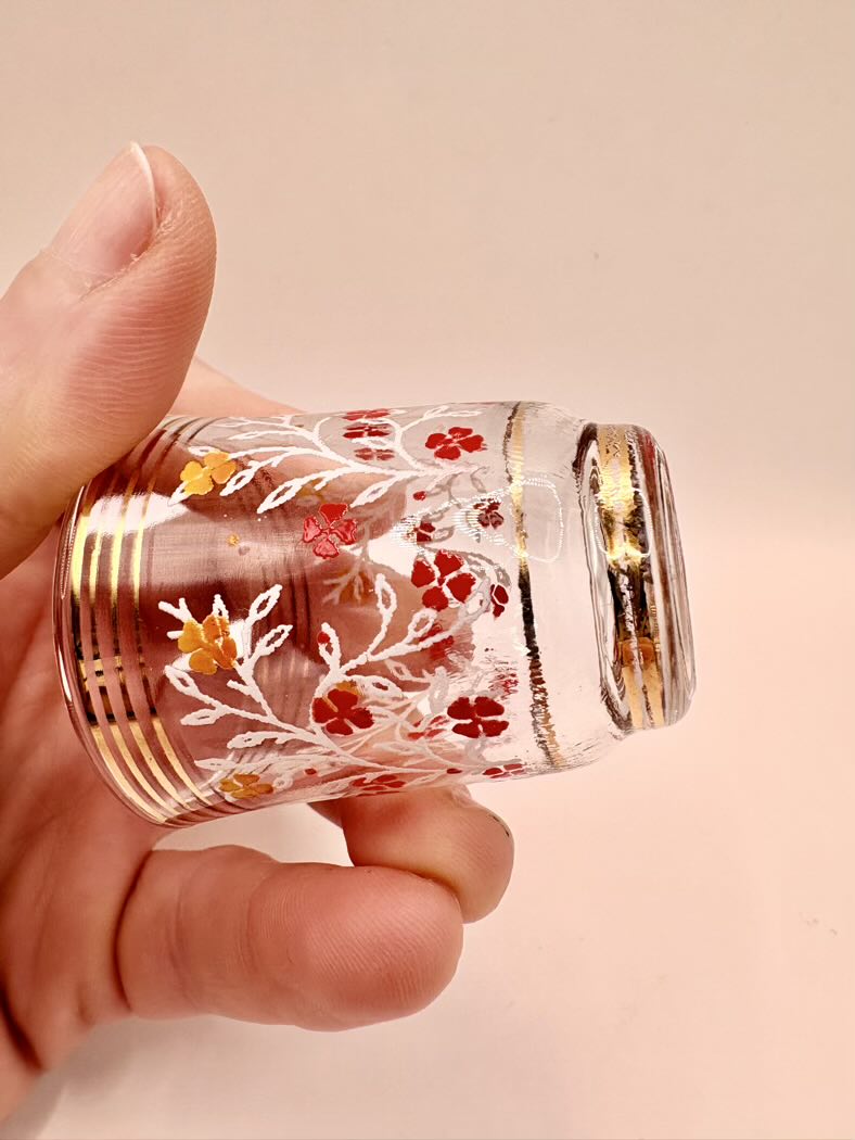 Hand holding a small glass container with floral designs and gold accents on a beige background