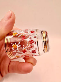 Hand holding a small glass container with floral designs and gold accents on a beige background
