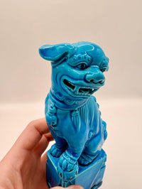Blue dog statue held in a hand against a beige background