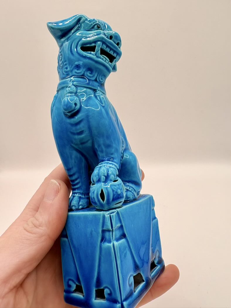 Blue ceramic dog statue held by a hand against a beige background