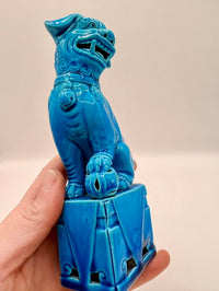 Blue ceramic dog statue held by a hand against a beige background