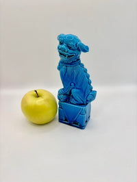 Blue ceramic dog figure next to a green apple on a white background