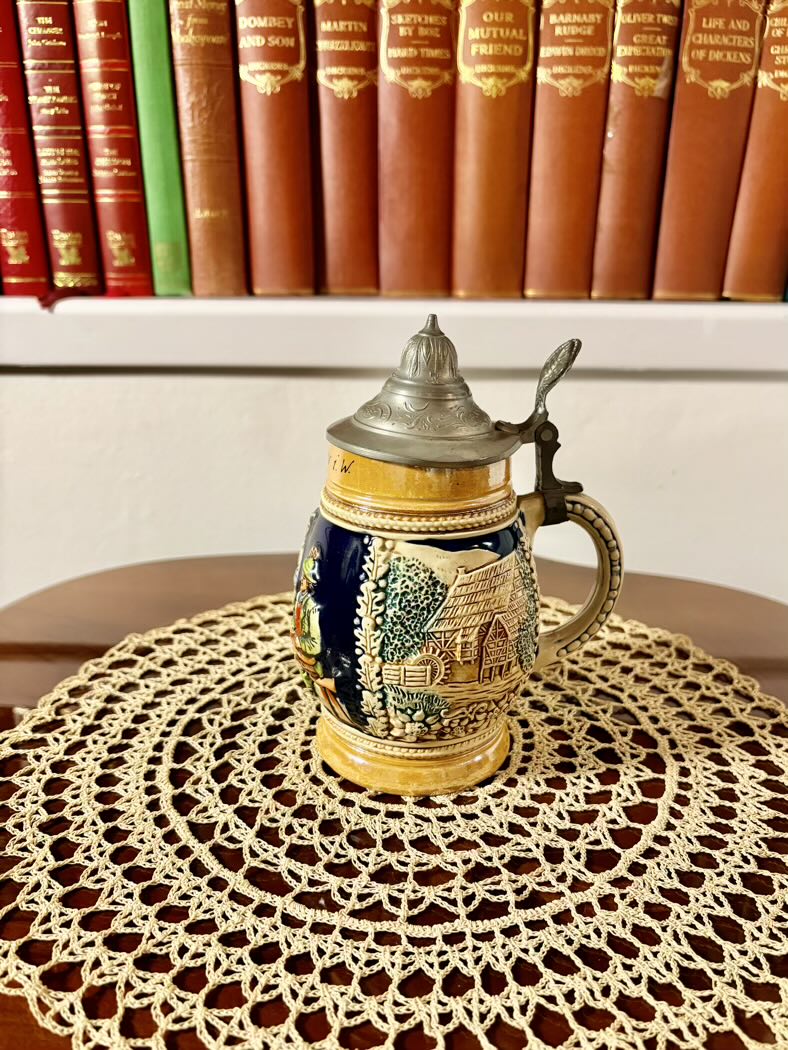 Decorative ceramic stein with lid on a lace doily in front of books