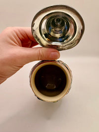 Hand holding a metallic object with a reflective surface on a beige background