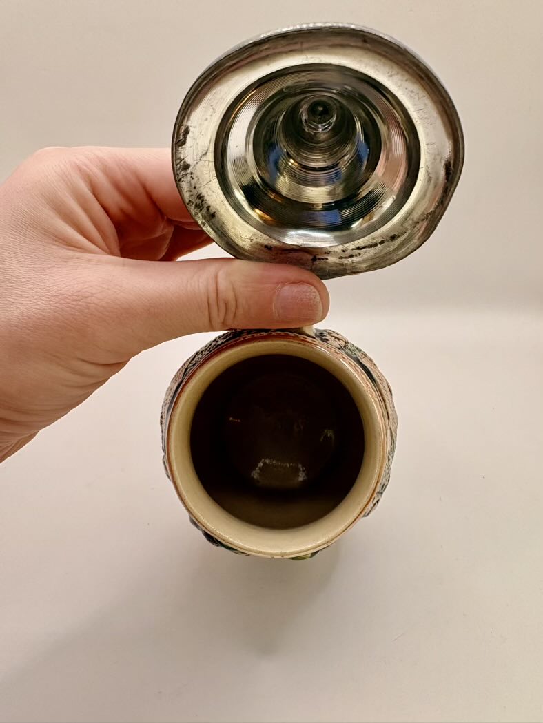 Hand holding a metallic object with a reflective surface on a beige background