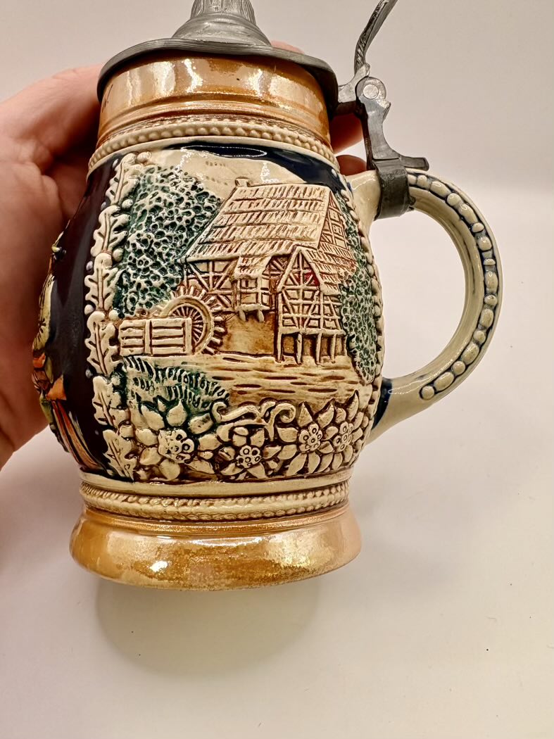 Decorative ceramic stein with a detailed design held by a hand on a white background
