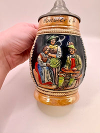 Decorative ceramic stein with painted scenes held by a hand on a light background