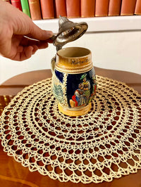 Decorative beer stein with intricate designs on a lace doily