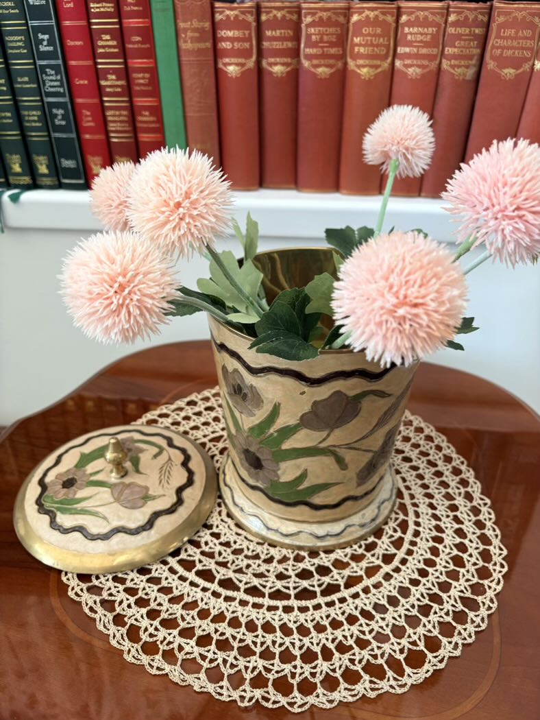 Decorative pot with pink flowers on a table with books in the background