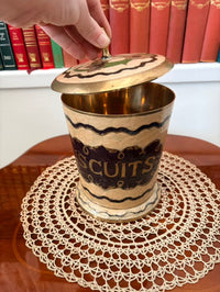 Decorative cookie jar with ' biscuits' text on a doily, with books in the background.