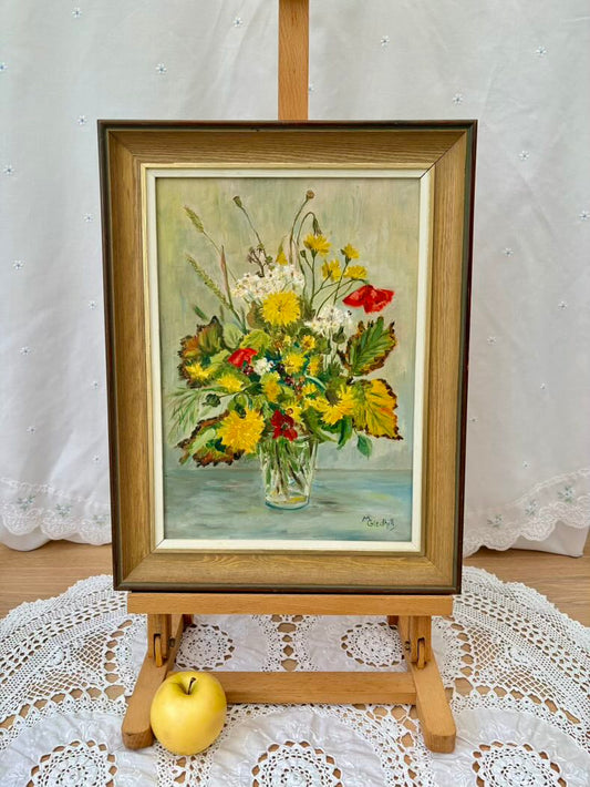 Framed painting of a floral arrangement on an easel with a white doily and yellow apple below.
