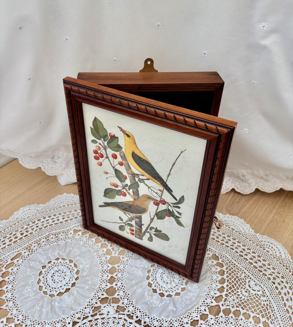 Framed artwork of birds on a branch with berries on a lace tablecloth.