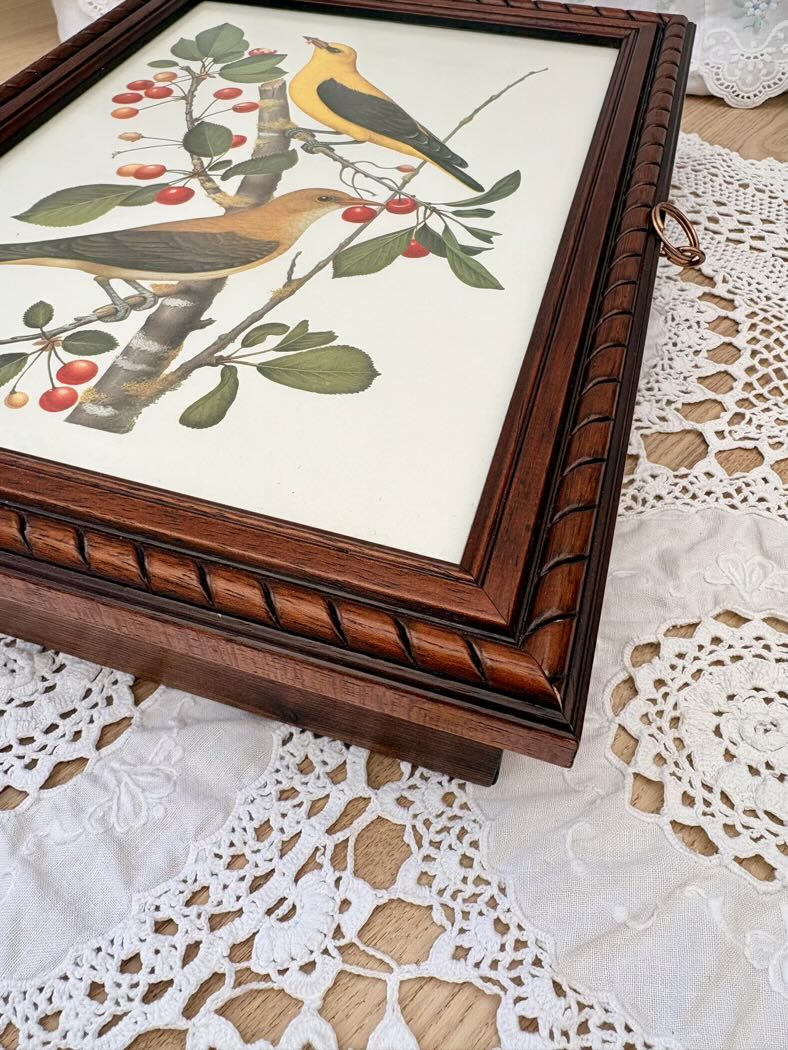 Framed artwork of birds and berries on a lace tablecloth