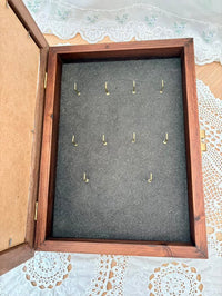 Wooden keys box with gray interior displaying gold hooks on a lace tablecloth.