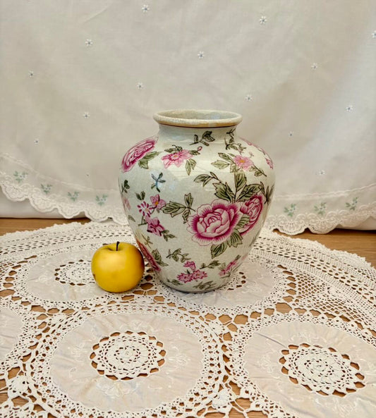 Decorative vase with floral patterns on a lace tablecloth with an apple beside it.