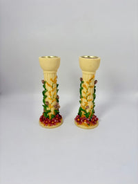 Two decorative candle holders with floral and fruit design on a light gray background
