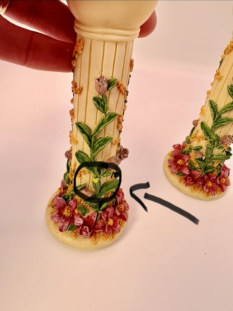 Decorative sandal with floral design held by a hand on a light pink background