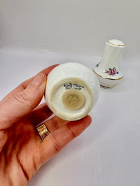 Hand holding a small white ceramic vase with 'Bone China England' marking, another similar vase in the background.