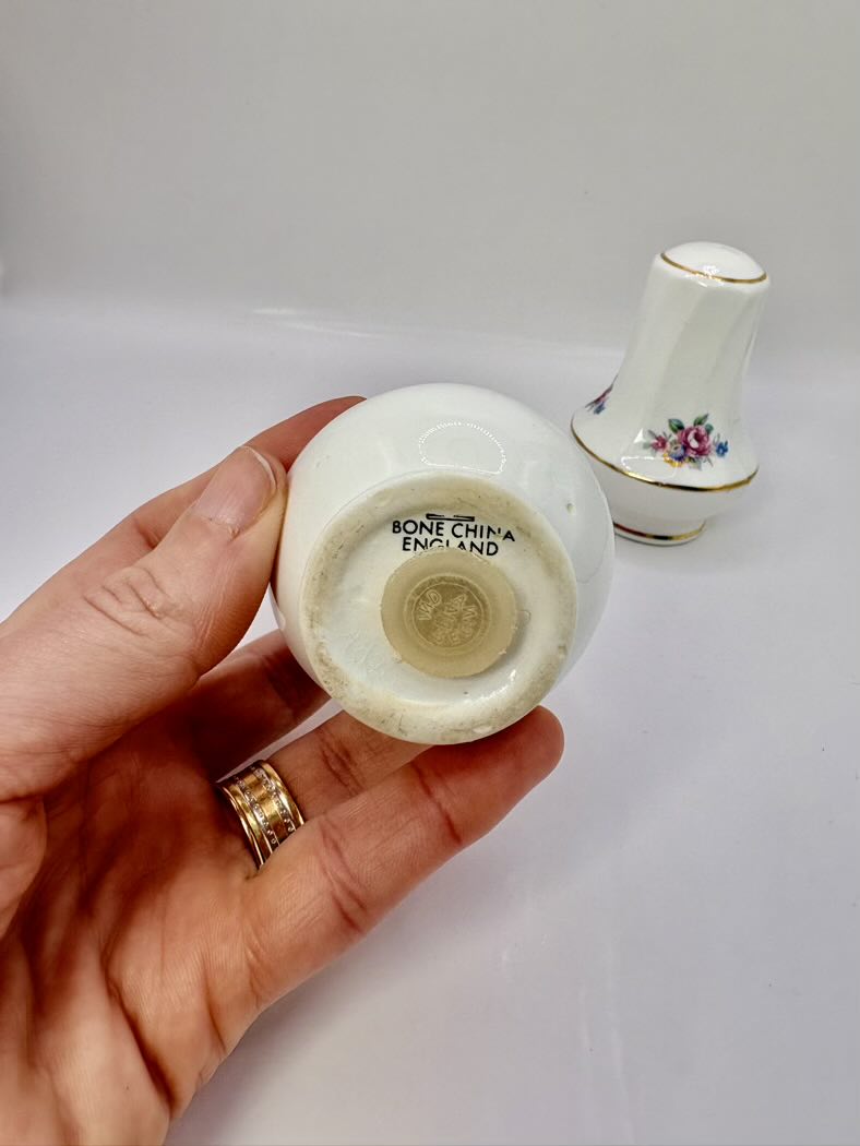 Hand holding a small white ceramic vase with 'Bone China England' marking, another similar vase in the background.