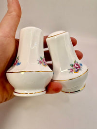 Two small white ceramic containers with floral designs held by a hand against a plain background