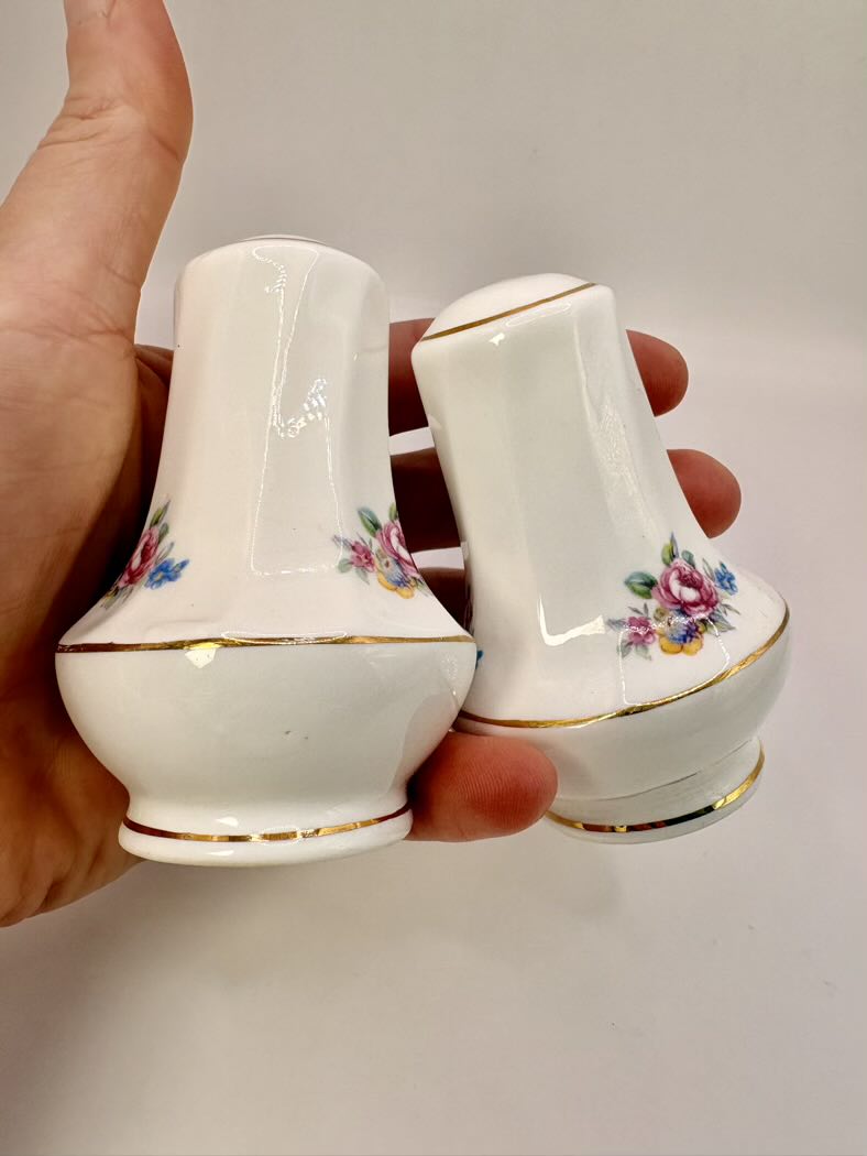 Two small white ceramic containers with floral designs held by a hand against a plain background