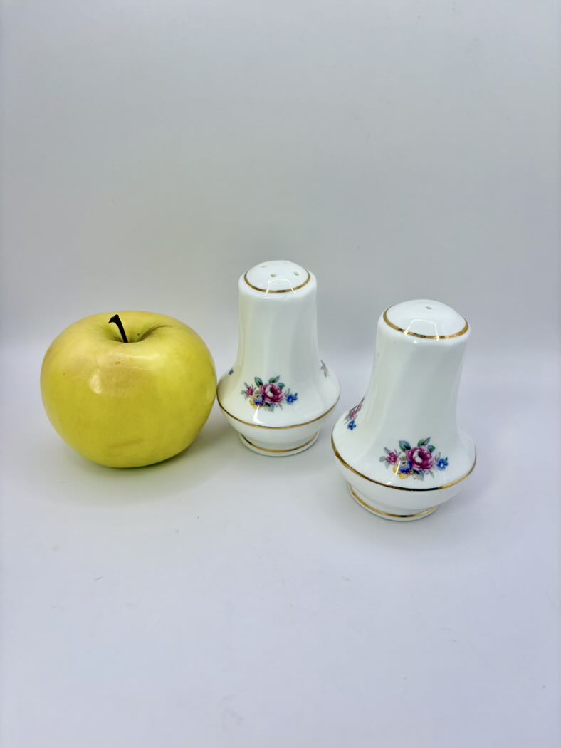 Two ceramic salt and pepper shakers with floral designs next to a yellow apple on a white background