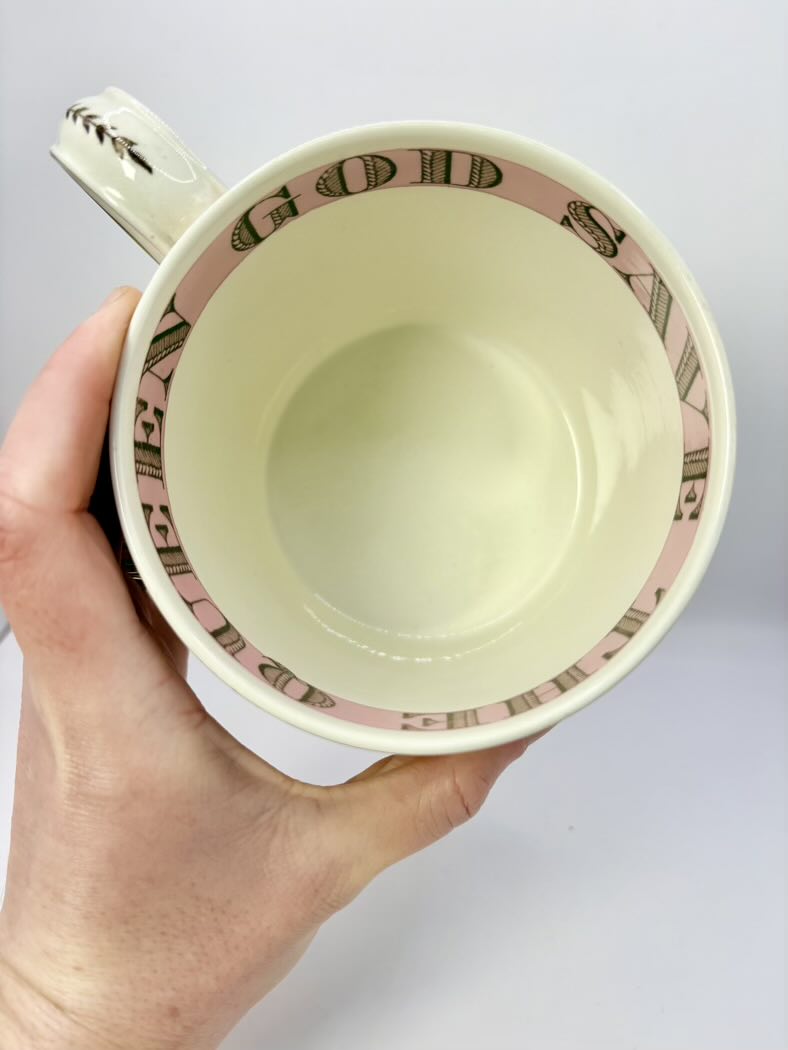 Hand holding a light beige mug with decorative rim against a white background