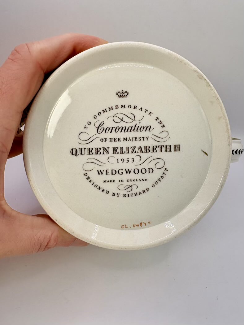Ceramic plate with Queen Elizabeth II commemoration text held by a hand on a white background