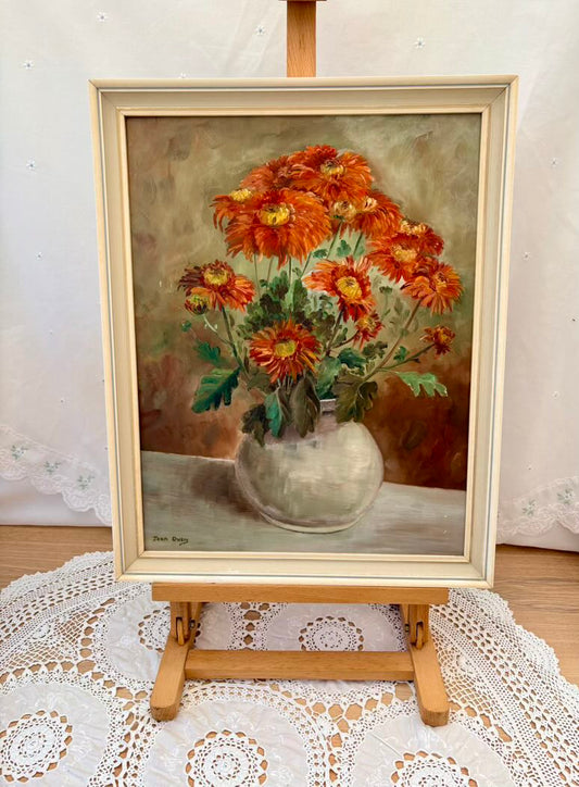 Framed painting of a bouquet of flowers on an easel with a lace tablecloth underneath.