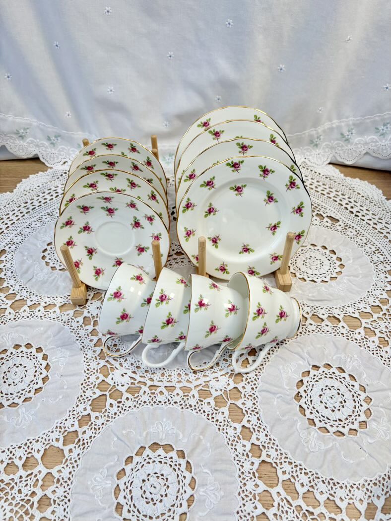 Set of ceramic teacups and saucers with floral design on a lace tablecloth.