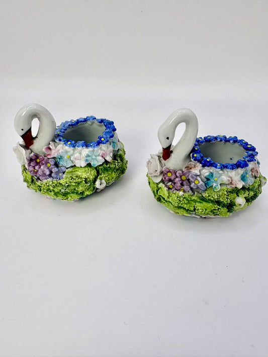 Two ceramic swan candle holders with floral designs on a white background