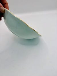 Ceramic bowl with gold rim held by a hand on a white background