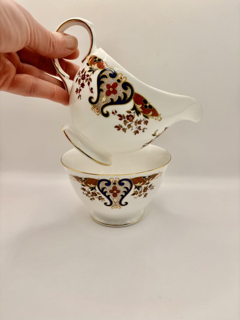 Decorative teacup and saucer with intricate patterns held by a hand on a light background