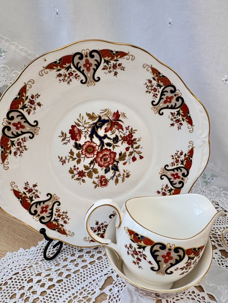 Decorative teacup and saucer with floral and paisley patterns on a lace tablecloth.