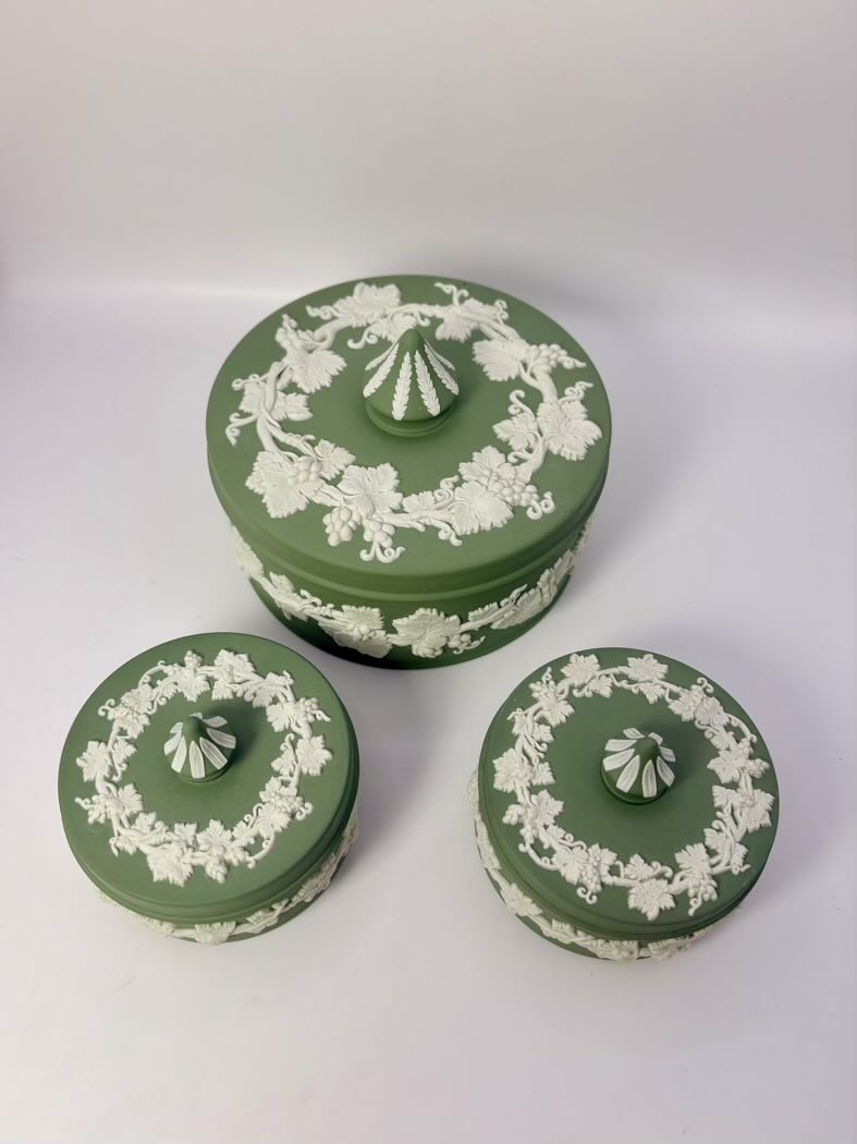 Set of three green ceramic jars with white floral patterns on a white background