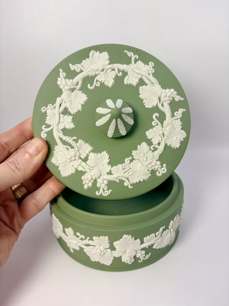 Green ceramic box with white floral patterns held by a hand on a white background