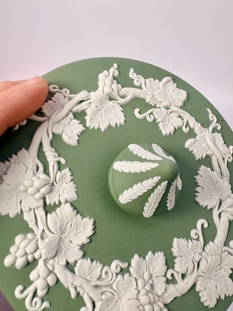 Decorative green plate with white floral patterns and a handprint design, held by a hand.